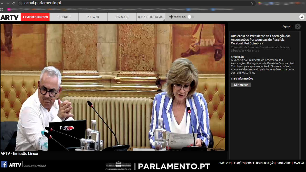 Captura de ecrã de emissão, online, do sítio do Parlamento. Na imagem, além do grafismo do sítio do Parlamento, surgem duas pessoas lado a lado – sendo que uma das pessoas aparenta estar a ler o que tem escrito ou impresso numa folha de papel.