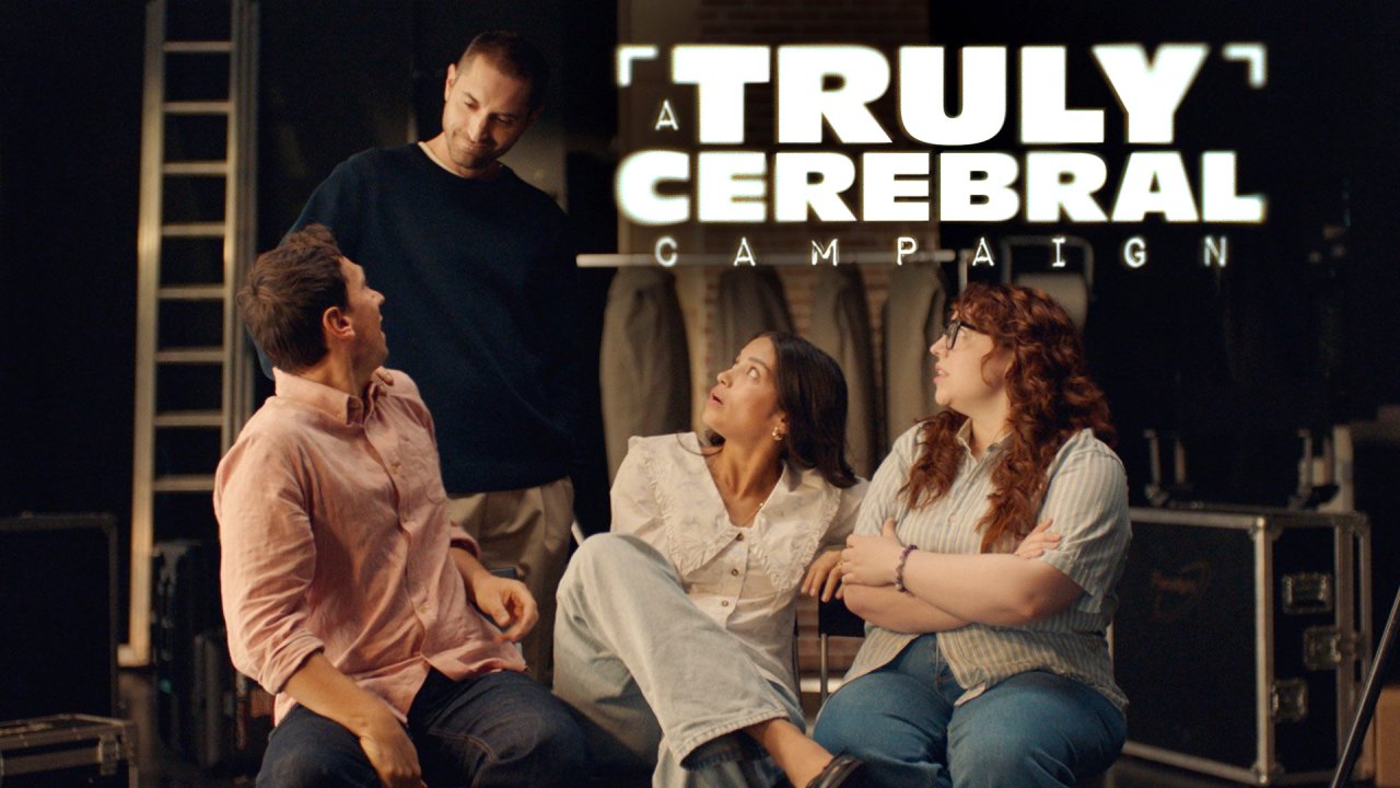 Grupo de quatro pessoas no que aparenta ser um palco ou estúdio. Uma pessoa está de pé e as restantes estão sentadas. A imagem foi sobreposta, na zona superior direita, com a expressão “A Truly Cerebral Campaign” em letras brancas e parcialmente desfocadas.