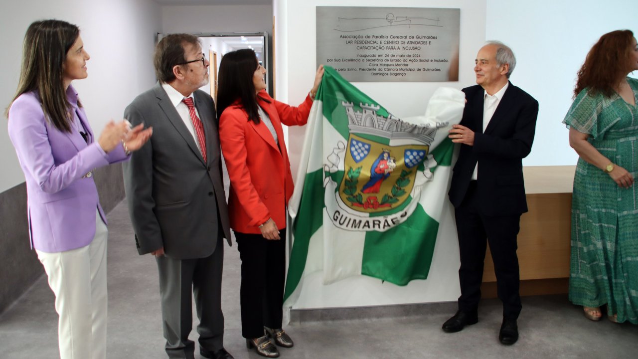 Duas pessoas retiram a bandeira (do Município de Guimarães) que cobria uma placa em metal. Ao lado outras três pessoas assistem ao momento.